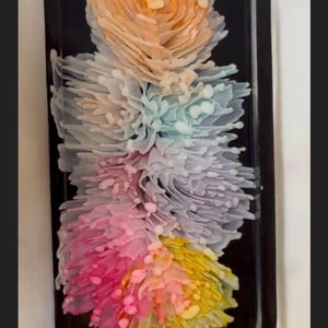 May include: A decorative black tray featuring a floral design in shades of orange, pink, yellow, blue, and white. The flowers have a layered, textured appearance, creating a 3D effect. The tray has a smooth, glossy finish.