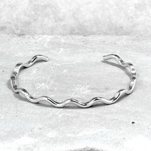 May include: A silver wavy cuff bracelet. The bracelet is made of a thin, flexible metal and has a simple, modern design.