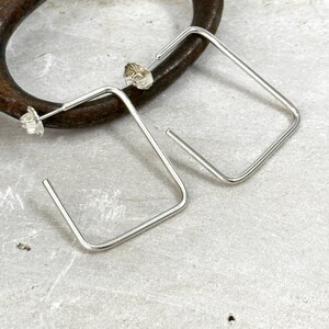 May include: A pair of silver square hoop earrings. The earrings are simple and modern in design.