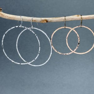 May include: Three pairs of hammered hoop earrings in silver and gold tones. The earrings are hanging from a branch.