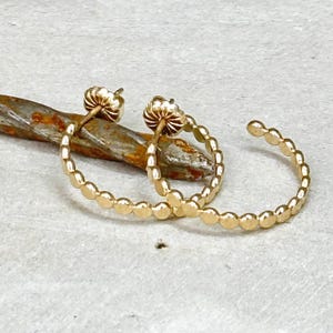 May include: A pair of gold hoop earrings with a beaded design. The earrings are made of small, round beads that are connected together to form a hoop shape.