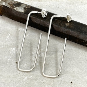 May include: A pair of silver rectangle shaped earrings with a simple design. The earrings are long and have a slightly curved shape.