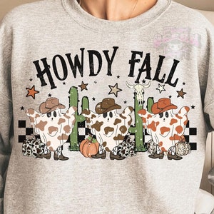 May include: A light gray sweatshirt with the words "HOWDY FALL" in black. The graphic features cartoon ghosts wearing cowboy hats and cowhide patterns, with cacti, stars, and a pumpkin.
