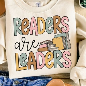 May include: A cream colored sweatshirt with the text "Readers are Leaders" in colorful letters. A stack of books is pictured next to the text.