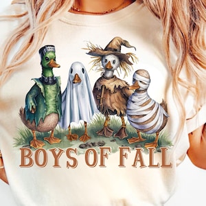 Pode incluir: Uma camiseta branca com um gráfico de quatro patos vestidos com fantasias de Halloween. Os patos são um Frankenstein, um fantasma, um espantalho e uma múmia. O texto "BOYS OF FALL" está impresso abaixo dos patos.