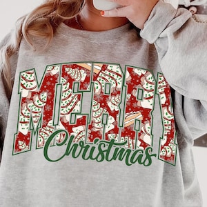 Pode incluir: Um moletom cinza com a frase "MERRY Christmas" em um design festivo. As letras são preenchidas com padrões de árvores de Natal em vermelho, verde e branco. O moletom é um estilo casual e confortável.