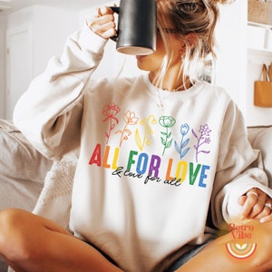 Puede incluir: Una sudadera blanca con un dise&ntilde;o de arco&iacute;ris con flores y el texto "ALL FOR LOVE & love for all".