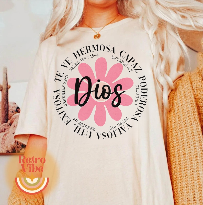 May include: A white t-shirt with a pink flower graphic and the text "Dios" in the center. The flower is surrounded by a circle of text in Spanish, including Bible verses.