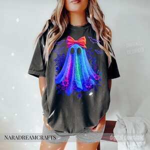 Peut inclure: T-shirt noir avec un motif de fant&ocirc;me color&eacute; orn&eacute; d'un n&oelig;ud, de fleurs et de chauves-souris. Le fant&ocirc;me est un m&eacute;lange vibrant de bleu, violet et vert. Le texte "NARADREAMCRAFTS" est en bas.