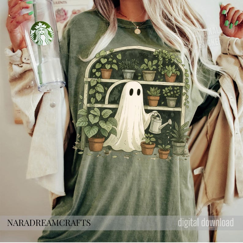 K&ouml;nnte beinhalten: Salbeigr&uuml;nes T-Shirt mit einer skurrilen Illustration eines Geistes, der Pflanzen in einem Gew&auml;chshaus gie&szlig;t. Das Design umfasst Topfpflanzen, eine Gie&szlig;kanne und den Text "NARADREAMCRAFTS" und "digital download".