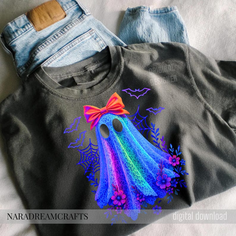 Peut inclure: T-shirt gris fonc&eacute; avec un motif de fant&ocirc;me color&eacute;, orn&eacute; d'un n&oelig;ud orange vif, de chauves-souris, de toiles d'araign&eacute;es et de fleurs violettes. Les textes "NARADREAMCRAFTS" et "digital download" sont visibles.