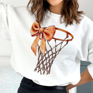 Op de afbeelding: Witte trui met een afbeelding van een basketbalring met een oranje strik.