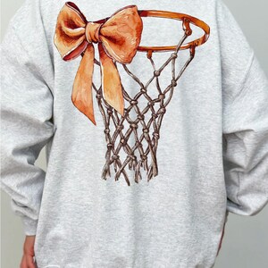 Op de afbeelding: Een grijs sweatshirt met een basketbalring en een grote oranje strik op de rug.