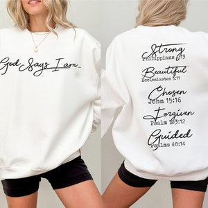 Może przedstawiać: Biała bluza z napisem "God Says I am..." z przodu i napisem "Strong Philippians 4:13, Beautiful Ecclesiastes 3:11, Chosen John 15:16, Forgiven Psalm 103:12, Guided Psalms 48:14" z tyłu.