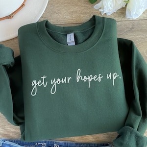 May include: A dark green sweatshirt with the text "get your hopes up." in white lettering.