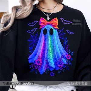 Peut inclure: Sweat-shirt noir avec un motif de fant&ocirc;me color&eacute;. Le fant&ocirc;me est un d&eacute;grad&eacute; arc-en-ciel avec un contour bleu, portant un n&oelig;ud orange. Le motif comprend des chauves-souris, des toiles d'araign&eacute;es et des fleurs. Le texte sur le sweat-shirt indique "ORIGINAL DESIGNER" et "digital download".