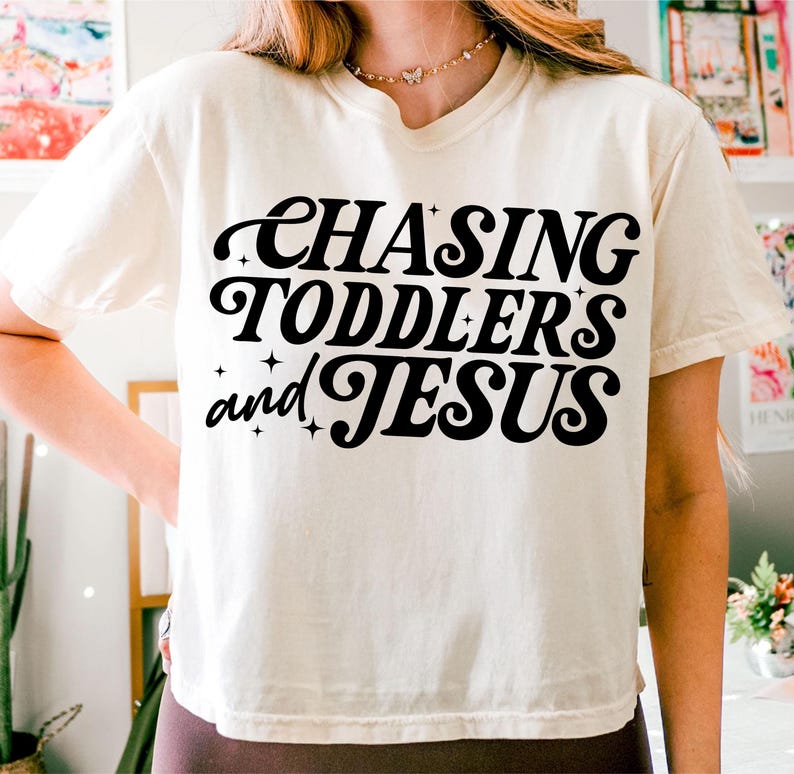 May include: A white cropped t-shirt with black text that reads "Chasing Toddlers and Jesus".