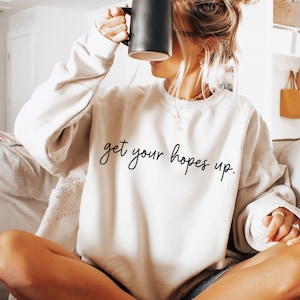May include: White sweatshirt with the text "get your hopes up." in black cursive writing.