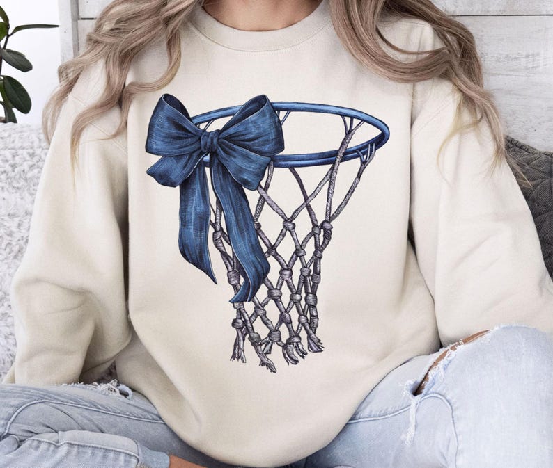 Peut inclure: Sweat-shirt cr&egrave;me avec une illustration d&eacute;taill&eacute;e d'un panier de basket et d'un grand n&oelig;ud bleu drap&eacute;. Le filet est finement dessin&eacute; et le n&oelig;ud ajoute un &eacute;l&eacute;ment d&eacute;coratif au th&egrave;me sportif. Le sweat-shirt est de couleur neutre.