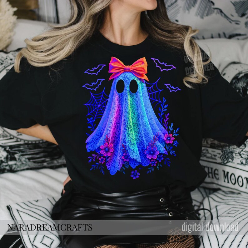 Peut inclure: T-shirt noir avec un motif de fant&ocirc;me color&eacute;, un n&oelig;ud, des fleurs et des chauves-souris. Le fant&ocirc;me est un m&eacute;lange vibrant de bleus, de violets et de verts. Le texte "NARADREAMCRAFTS" est en bas du t-shirt.