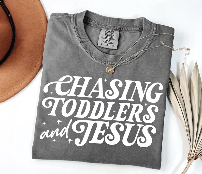 May include: A gray t-shirt with the text "Chasing Toddlers and Jesus" in white retro-style lettering.