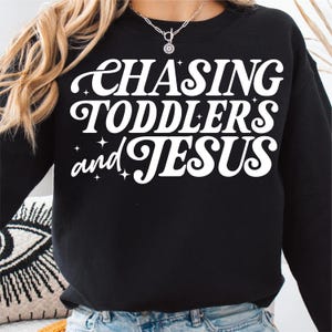 May include: Black sweatshirt with white text that reads "Chasing Toddlers and Jesus" in a retro font.