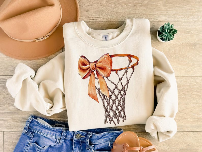 Op de afbeelding: Een cr&egrave;mekleurig sweatshirt met een bruine en oranje strik om een ​​basketbalring-afbeelding.