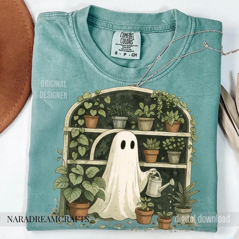 K&ouml;nnte beinhalten: Ein teal Comfort Colors T-Shirt mit einer skurrilen Illustration eines Geistes, der Pflanzen in einem Gew&auml;chshaus gie&szlig;t. Das Design zeigt Topfpflanzen, eine Gie&szlig;kanne und die Texte "NARADREAMCRAFTS" und "digital download".