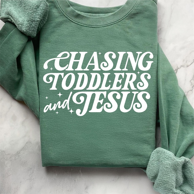 May include: A green sweatshirt with the text "CHASING TODDLERS and JESUS" in white retro-style lettering.