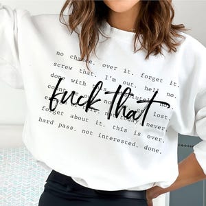 May include: White sweatshirt with the phrase "fuck that" in a bold, black script. Surrounding the phrase are smaller black text phrases like "no chance," "forget it," and "hard pass." The sweatshirt is a casual, comfortable style.
