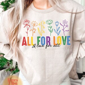 Puede incluir: Una sudadera beige con un dise&ntilde;o de arco&iacute;ris de flores y el texto "All for Love & love for all".