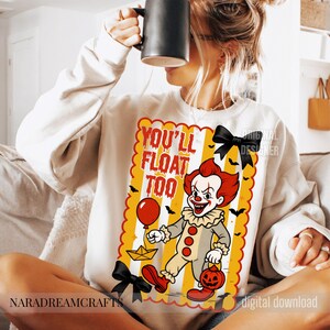 Op de afbeelding: Cr&egrave;mekleurige sweatshirt met een Halloween-thema. De afbeelding toont een clown met rood haar, de tekst "YOU'LL FLOAT TOO", een rode ballon en een pompoen. Zwarte vleermuizen en een papieren boot zijn ook inbegrepen.