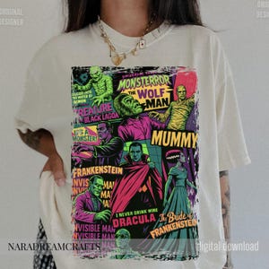 May include: Cream-colored t-shirt featuring a colorful graphic of classic Universal Monsters. The design includes images of the Wolf Man, Dracula, Frankenstein, and the Mummy, with text like "Monsteror" and "Creature from the Black Lagoon."