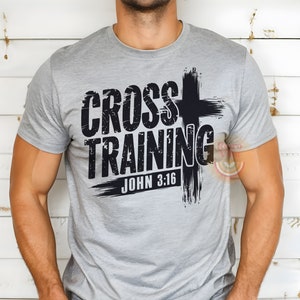 May include: A gray t-shirt with the words "CROSS TRAINING" in a distressed black font, accompanied by a black cross graphic. The text "JOHN 3:16" is printed below. The shirt is made of a soft material.