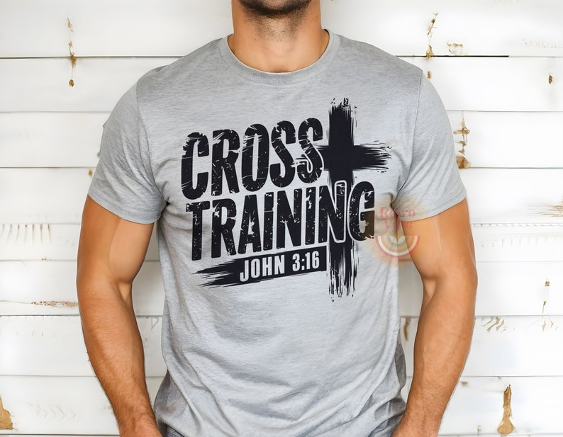 May include: A gray t-shirt with the words "CROSS TRAINING" in a distressed black font, accompanied by a black cross graphic. The text "JOHN 3:16" is printed below. The shirt is made of a soft material.