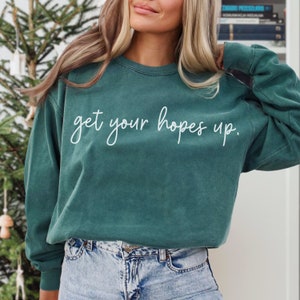 May include: A teal green sweatshirt with the text "get your hopes up" in white lettering.