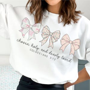 May include: White sweatshirt with three illustrated bows in pink and floral patterns. The text "chosen holy and dearly loved" and "COLOSSIANS 3:12" are printed below the bows.