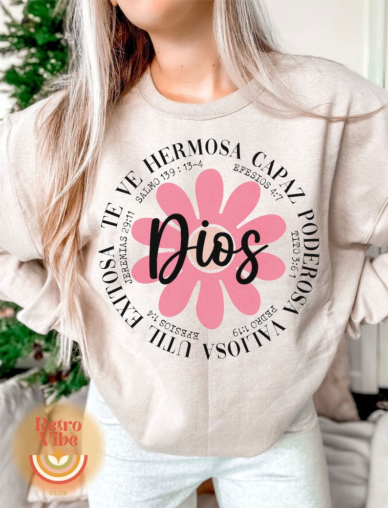 May include: A beige sweatshirt with a pink flower graphic and the text "Dios" in the center. The text around the flower includes bible verses in Spanish.