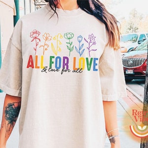 Puede incluir: Una camiseta blanca con un dise&ntilde;o de arco&iacute;ris de flores y el texto "ALL FOR LOVE & love for all".
