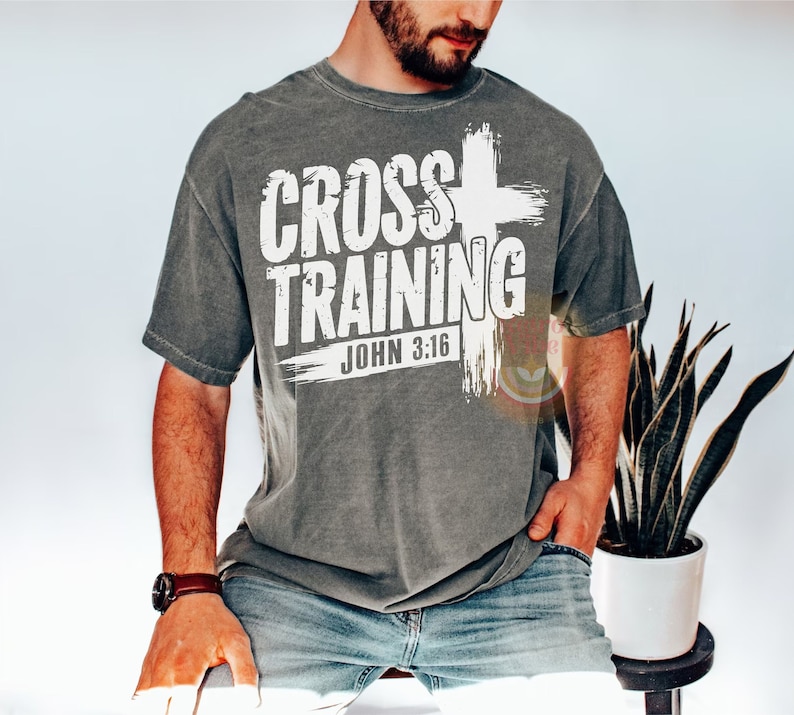 May include: Gray t-shirt with the words "CROSS TRAINING" and "JOHN 3:16" in white block letters. A white cross graphic is on the right side of the text. The shirt is worn by a person.