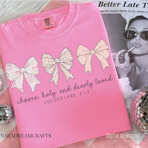May include: A pink Comfort Colors t-shirt featuring three decorative bows with floral and patterned designs. The text "chosen holy and dearly loved COLOSSIANS 3:12" is printed below the bows. The shirt has a crew neck.
