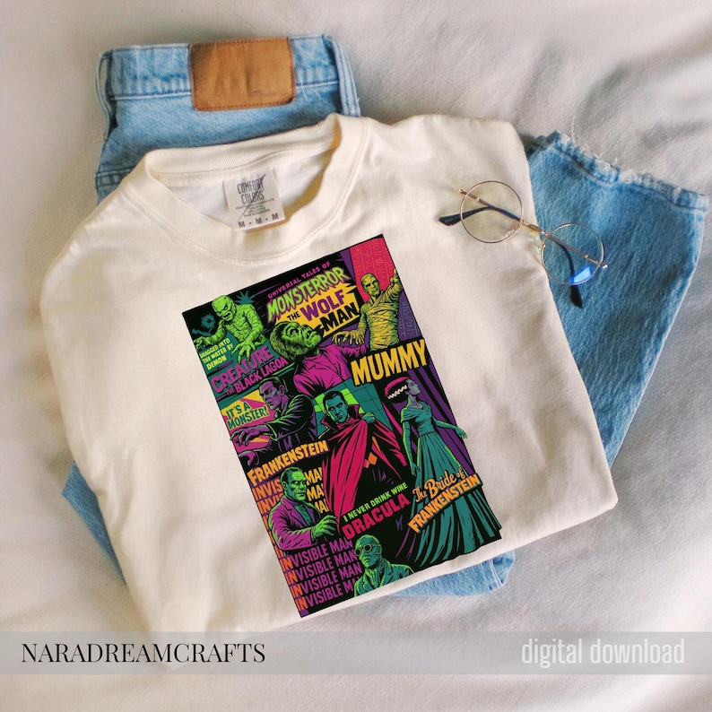 May include: Cream-colored t-shirt featuring a colorful graphic of classic Universal Monsters movie posters. The design includes images of the Wolf Man, Mummy, Dracula, and Frankenstein. The shirt is paired with blue jeans and glasses.