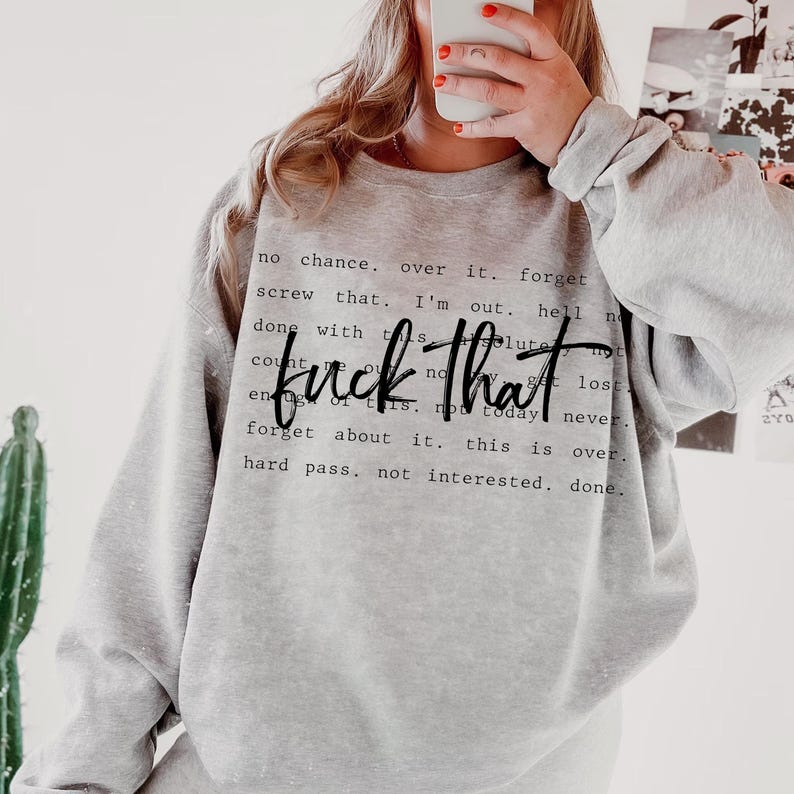 May include: A light gray sweatshirt with the phrase "fuck that" in a bold, black script. Surrounding the phrase are smaller lines of text. The sweatshirt has long sleeves and a crew neck.