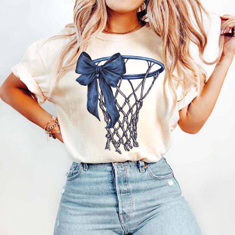 Peut inclure: T-shirt cr&egrave;me avec un motif de filet de basket-ball bleu marine orn&eacute; d'un grand n&oelig;ud. Le filet est d&eacute;taill&eacute; avec un motif tiss&eacute;, et le n&oelig;ud ajoute un &eacute;l&eacute;ment d&eacute;coratif. Le t-shirt est associ&eacute; &agrave; un jean en denim bleu clair.