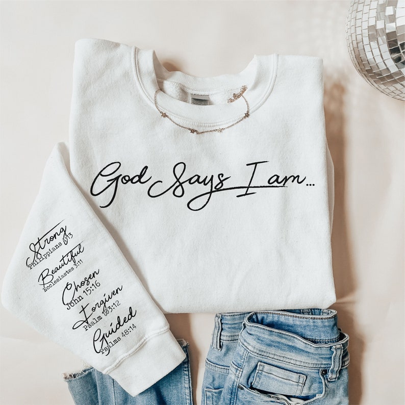 Może przedstawiać: Biała bluza z nadrukiem "God Says I am..." na przodzie. Lewy rękaw ma nadrukowane słowa "Strong, Beautiful, Chosen, Forgiven, Guided" wraz z odpowiadającymi im wersetami biblijnymi.
