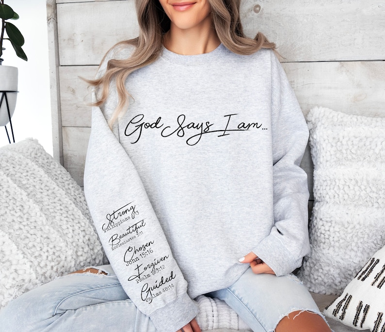 Może przedstawiać: Szara bluza z nadrukiem "God Says I am..." na przodzie. Lewy rękaw ma pionowo nadrukowane słowa "Strong, Beautiful, Chosen, Forgiven, Guided" wraz z odpowiadającymi im wersetami biblijnymi.