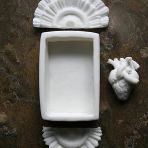 May include: White ceramic heart-shaped box with a removable lid. The lid is decorated with a fan-shaped design. The box is divided into three sections.