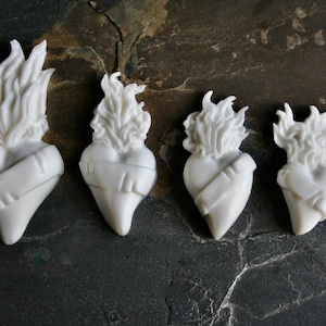 May include: Four white ceramic heart sculptures with flames on top. The hearts are different sizes and are arranged in a row from largest to smallest.