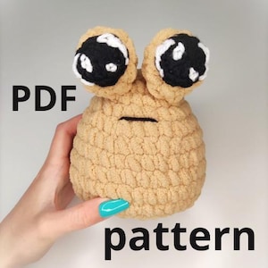 May include: A crochet pattern for a tan amigurumi toy with black eyes and white accents. The pattern is available as a PDF download.