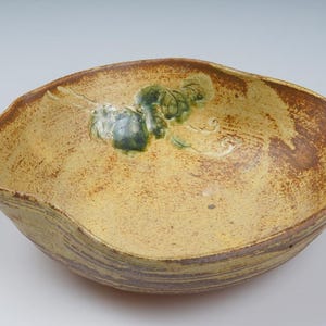 May include: A large, yellow ceramic bowl with a wavy rim and a green and white floral design. The bowl has a rustic, handmade look.